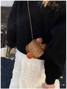 Dettaglio della borsa a tracolla marrone con mini orsetto e pompon arancione