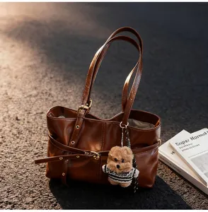 Détail du sac cabas en cuir marron avec sangle décorative et breloque ours en peluche