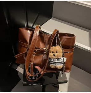 Gros plan du sac cabas en cuir marron foncé avec un petit pendentif ours en peluche