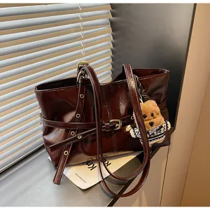 Détail d'un grand sac cabas en cuir ciré bordeaux brillant avec un joli pendentif ours