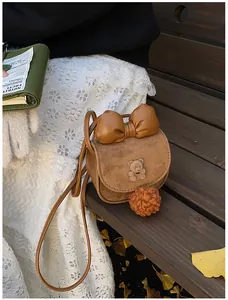 Dettaglio della borsa a tracolla per bambini marrone con orsetto e fiocco su panca di legno