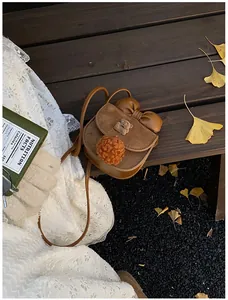 Borsa a tracolla marrone per bambina con fiocco e orsetto su una panca in legno