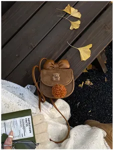 Dettaglio borsa a tracolla marrone scamosciata per bambini con orso, fiocco e foglie autunnali