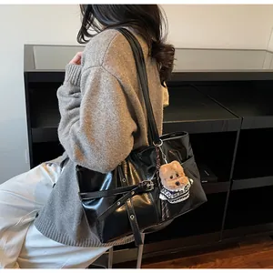 Détail du sac cabas noir en similicuir brillant avec boucle décorative et breloque ours à l'épaule