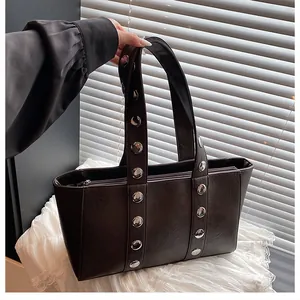 Close-up of a dark brown faux leather tote bag with silver metal studs and zipper closure