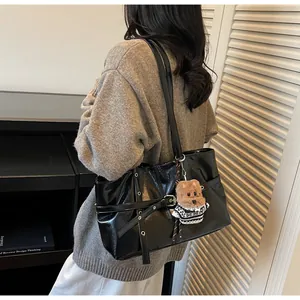 Détail du sac cabas noir brillant avec œillets métalliques et breloque ours en peluche