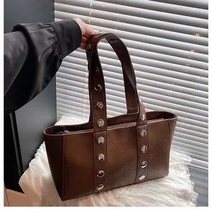 Macro detail of dark brown tote bag featuring silver rivet studs and a smooth zipper closure