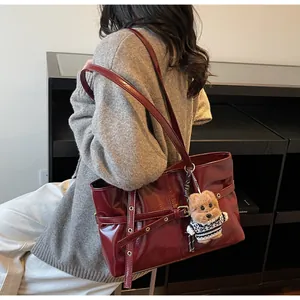 Détail d'un cabas en cuir bordeaux avec œillets métalliques et breloque ours sur l'épaule