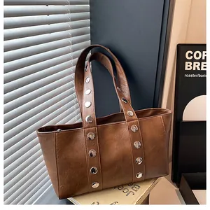 Close-up of brown textured leather tote bag featuring modern silver metal rivet details
