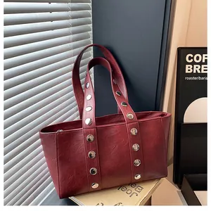 Detail of red faux leather tote bag featuring stylish silver rivets on dual shoulder straps