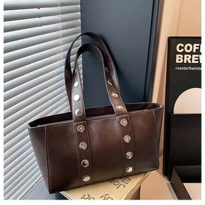 Detail of dark brown leather tote bag with silver metal rivets and textured finish