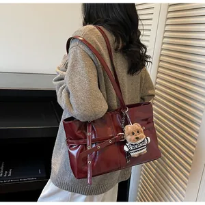 Détail du sac cabas en cuir ciré bordeaux avec boucles décoratives et breloque ours