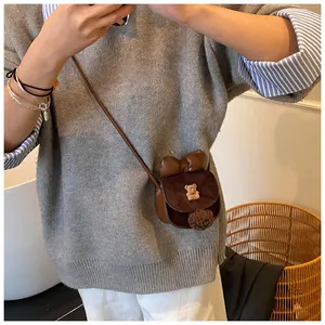 Dettaglio mini borsa a tracolla marrone con fiocco, stemma a orso e ciondolo a pompon