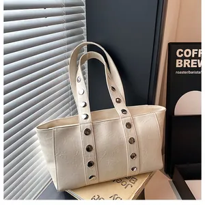 Detail of beige tote bag featuring silver studs on shoulder straps with soft shadow texture