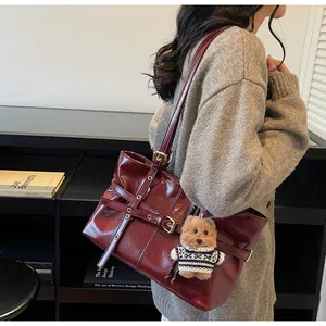 Détail du sac fourre-tout en cuir ciré rouge foncé avec boucles argentées et breloque ours