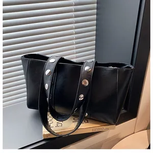 Detail of black tote bag with silver metal rivets on strap against window light