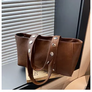 Detail of dark brown leather tote featuring large silver metal rivets on the wide strap