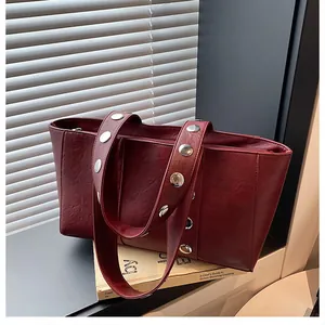 Detailed close-up of dark red faux leather bag with oversized silver metallic rivets on straps
