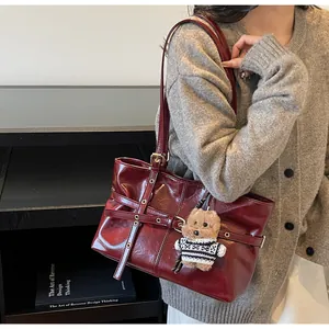 Gros plan d'un sac cabas en cuir ciré rouge foncé avec ceintures à œillets et charm ours