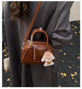 Brown leather Boston bag with plush puppy charm and checkered ribbon on autumn background