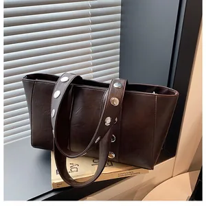 Detail of dark brown faux leather tote bag featuring large silver metal rivets on straps