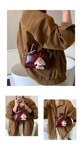 Detail of burgundy Boston bag with a cute puppy plush charm and ribbon handle