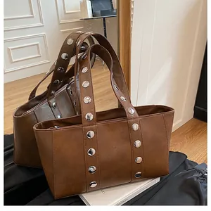 Detail of dark brown leather tote bag with oversized silver rivets in industrial style
