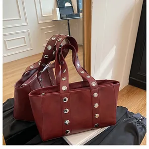 Detail view of burgundy tote with silver rivets and polished zipper closure in mirror reflection