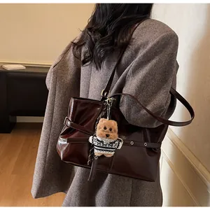 Détail du cabas marron brillant avec sangle à rivets et pendentif ourson en peluche