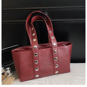 Detail of deep red tote bag with silver metal rivets on a professional office desk