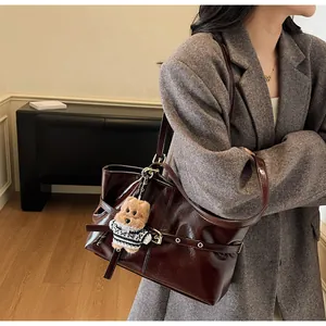 Détail d'un sac cabas en cuir ciré marron rouge foncé avec un porte-clés ours en peluche