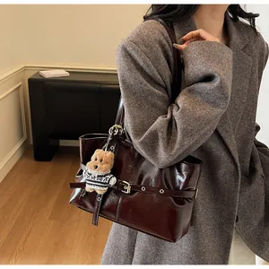 Détail d'un sac cabas en cuir ciré marron foncé avec boucle dorée et bijou d'ours