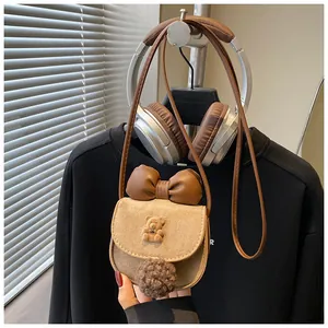 Dettaglio borsa a tracolla marrone per bambini con orsetto di peluche, fiocco e pompon