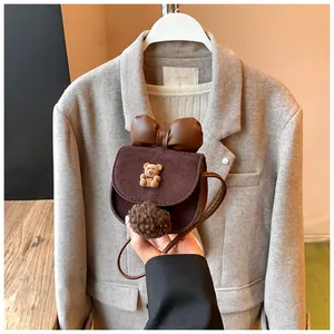 Dettaglio di una mini borsa a tracolla in pelle scamosciata marrone con orso e fiocco