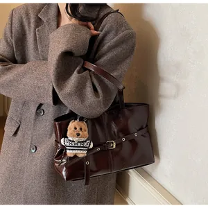 Détail du sac cabas marron brillant avec boucle et charm d'ours sur manteau gris