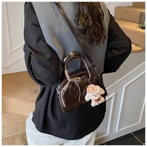 Close-up of brown polished Boston bag with plaid ribbon and white puppy plush keychain