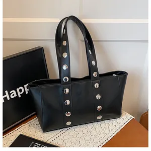 Detail of black faux leather tote bag showing silver rivets on dual shoulder straps