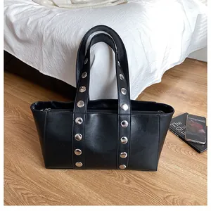 Close-up of a black glossy PU leather tote bag with vertical silver metal rivets