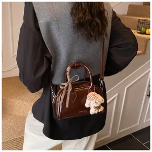Detail view of brown glossy leather bag with ribbon bow and plush dog charm accessory