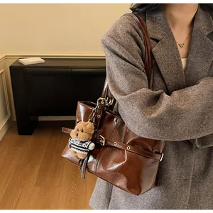 Détail du sac cabas en cuir ciré avec un charm ours en peluche et des boucles dorées