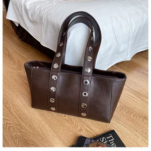 Close-up of dark brown tote bag featuring shiny faux leather and silver metal rivets