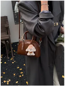 Detail of vintage brown leather pillow bag with plush dog charm and scarf in autumn setting