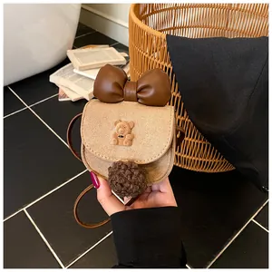 Dettaglio della borsa a tracolla kaki scamosciata per bambini con fiocco e orsetto peluche