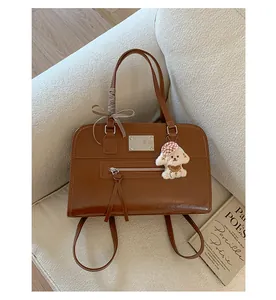 Detail of vintage brown leather tote bag with bow and plush puppy charm on a sofa