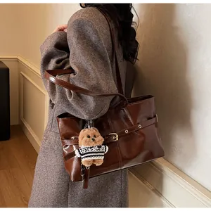 Détail du grand sac cabas en cuir marron avec breloque d'ours sur un manteau