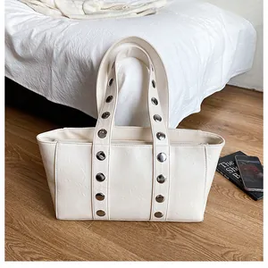 Detail of cream faux leather tote bag featuring silver rivets on a minimalist shoulder strap