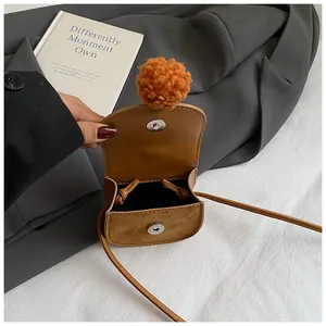 Dettaglio della borsa a tracolla in pelle marrone con chiusura magnetica e pompon arancione