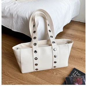 Close-up of cream tote bag featuring textured leather and large silver metal rivets