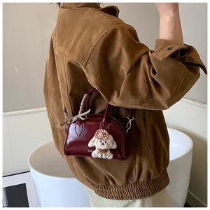 Detail of burgundy leather boston bag with plaid bow and plush dog charm accessory