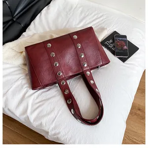 Detail of burgundy PU leather tote with silver metal rivets on white bedding